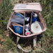 Boîte de transport pliable avec une armature métallique contenant des équipements de camping, posée sur l'herbe.