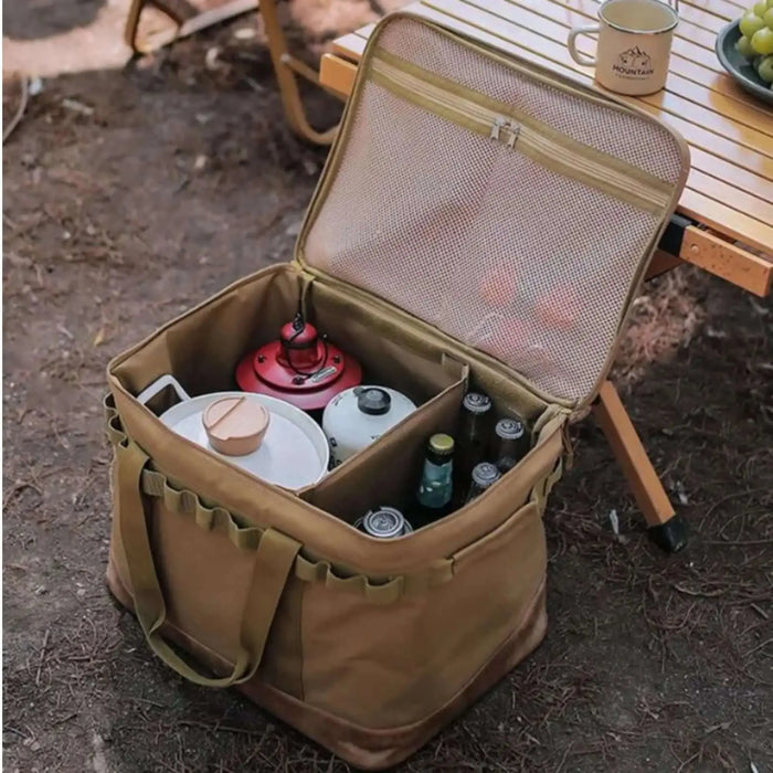 Boîte de transport pliable en toile avec armature métallique, remplie d'articles de camping, ouverte sur un sol forestier.