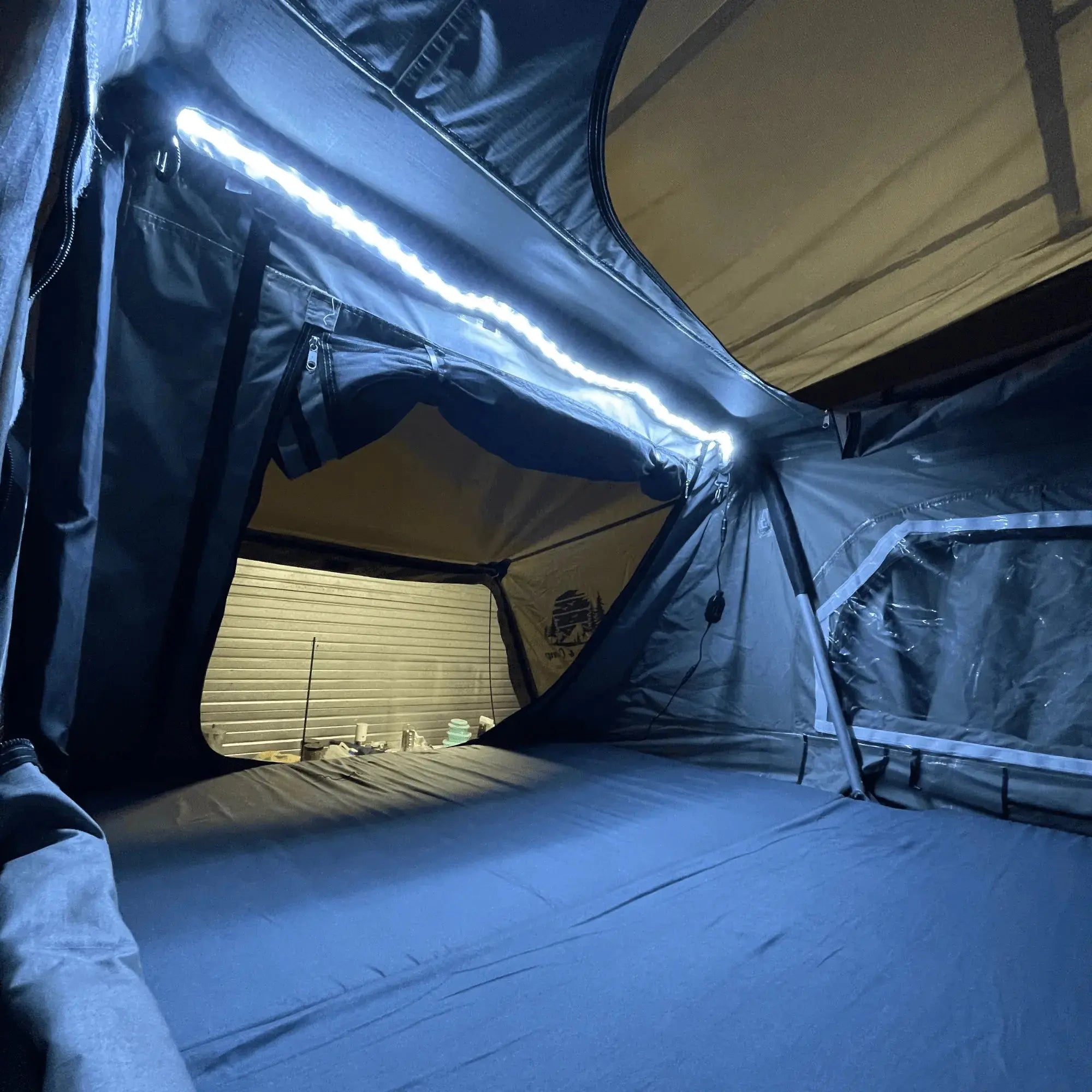 Vue intérieure d'un matelas de tente de toit gris pour 3 à 5 personnes, avec un éclairage LED, offrant un confort de sommeil en camping.
