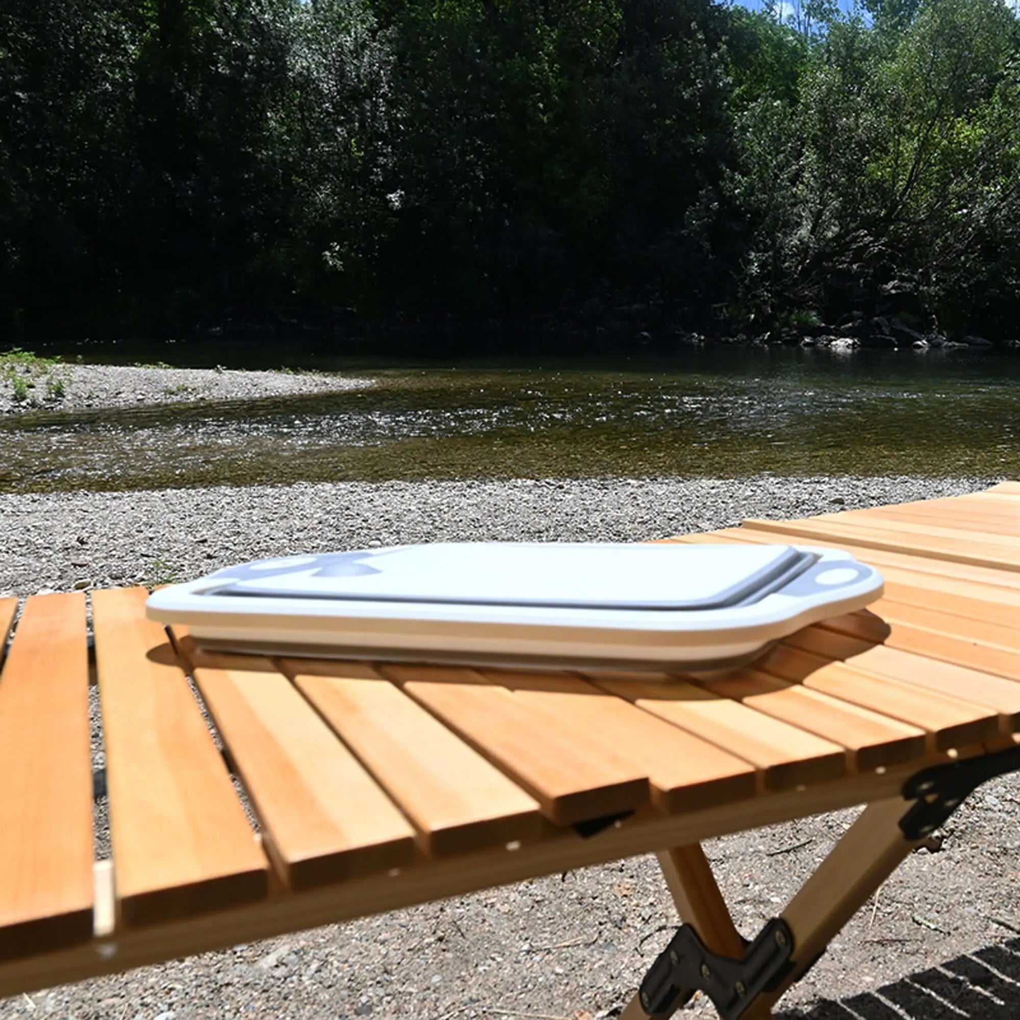 Portable silicone collapsible sink and cutting board on a foldable table by a river for camping use.