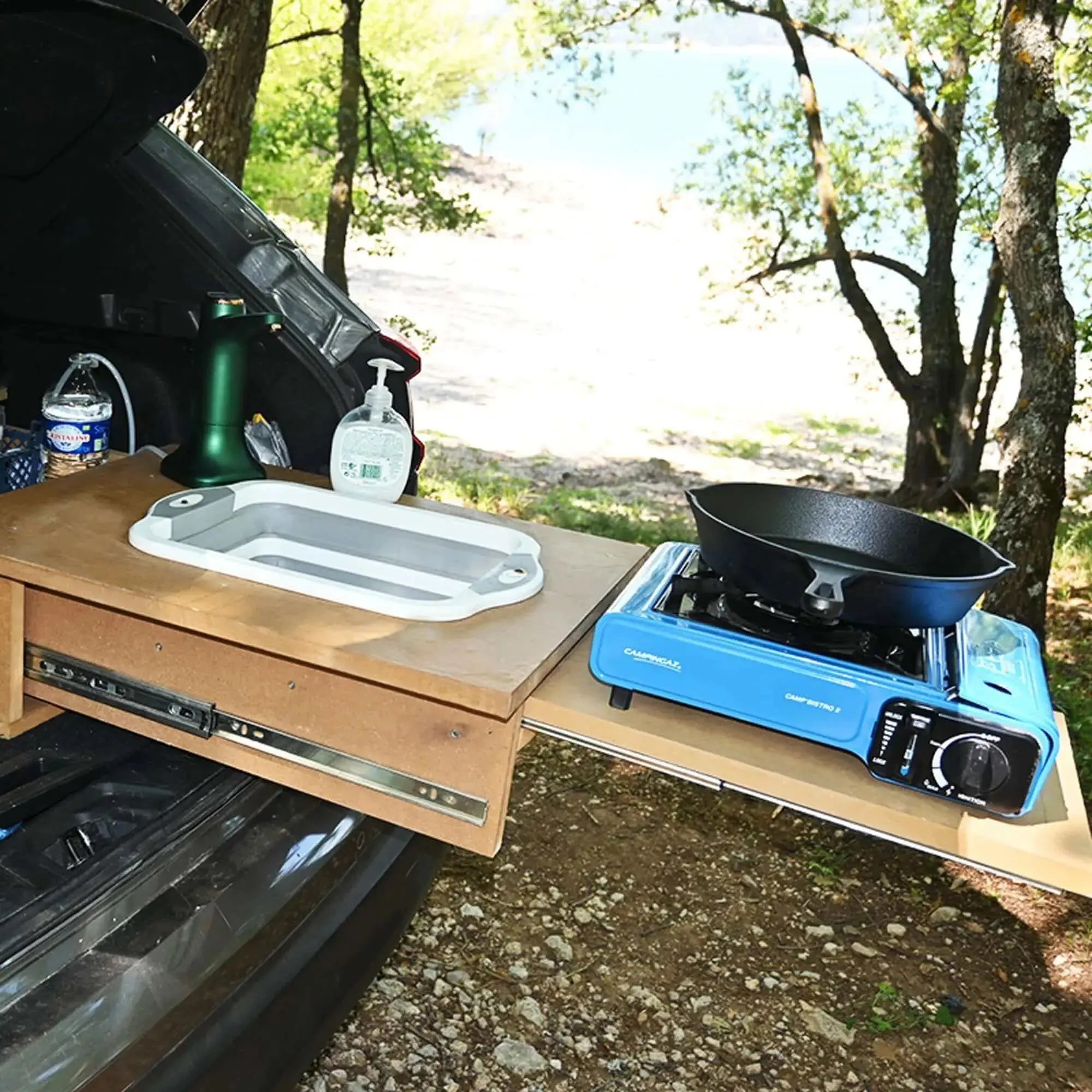 Portable camping kitchen setup with sink and gas stove on a sliding drawer table in the outdoors.