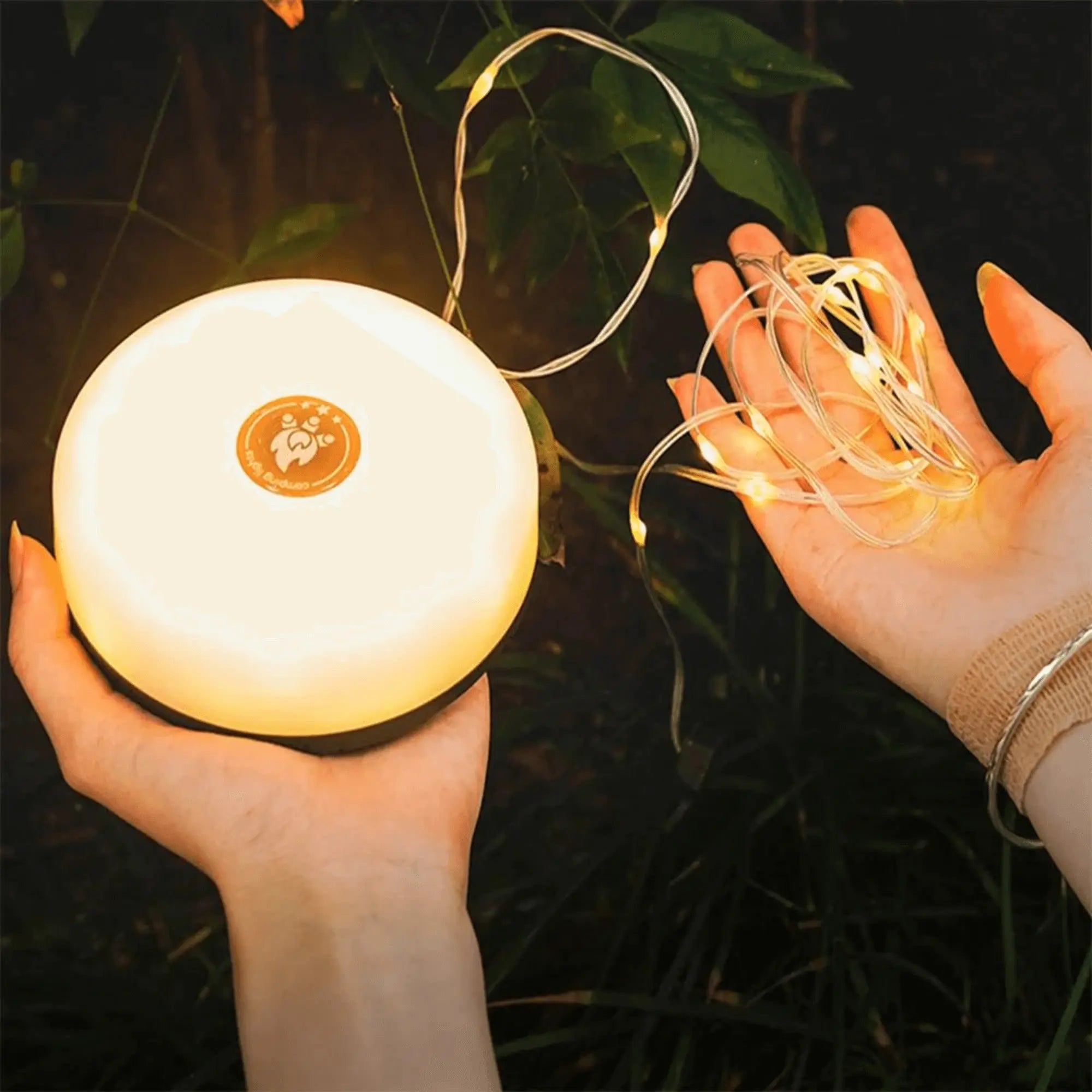 Hands holding portable string lights and a glowing lantern for outdoor use.