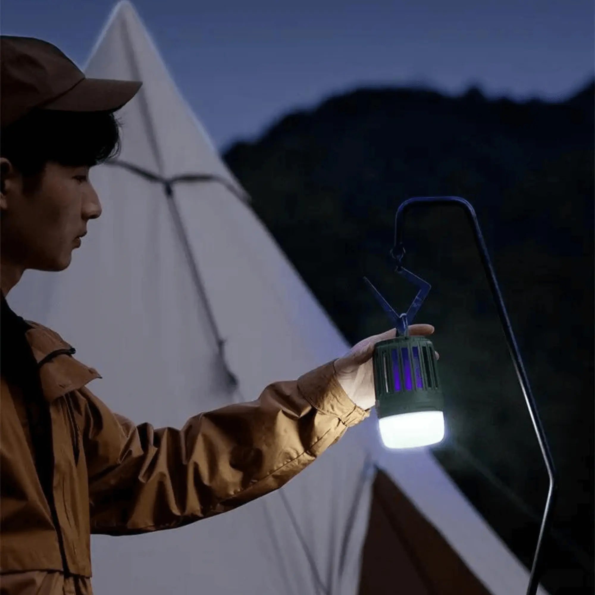 Lampe anti-moustique multifonction éclairant un camp de nuit, utilisée par un campeur devant une tente. Idéal pour soirées en plein air.