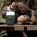 Lampe anti-moustiques multifonction éclairant une table de camping pendant que des personnes préparent à manger, idéale pour les aventures en plein air.