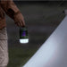 Une personne tenant une lampe multifonction contre les moustiques illuminant une aire de camping, mettant en valeur son design portable et protecteur.