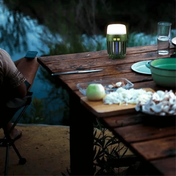 Lampe anti-moustique multifonction éclairant une table de camping au bord de l'eau, idéale pour protéger vos soirées en plein air.