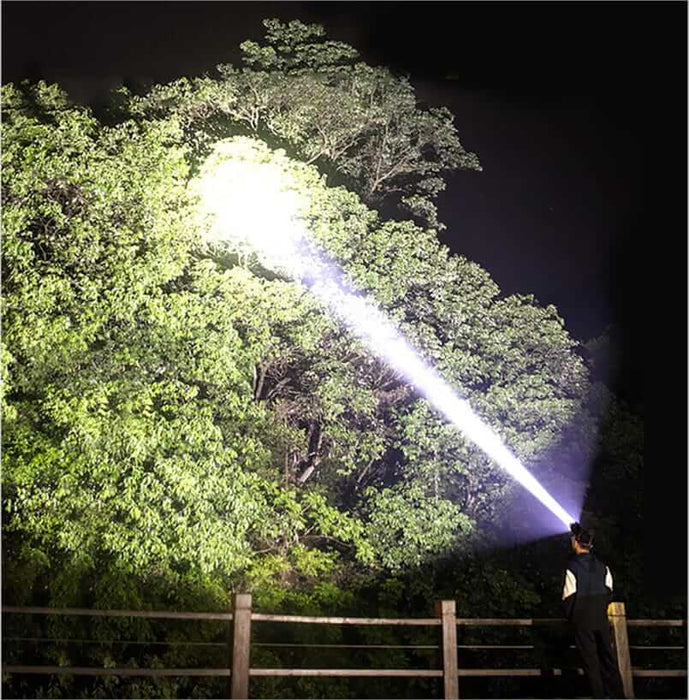 Lampe frontale haute puissance illuminant la forêt de nuit, idéale pour le camping sauvage et les activités de plein air avec 90 000 lumens.