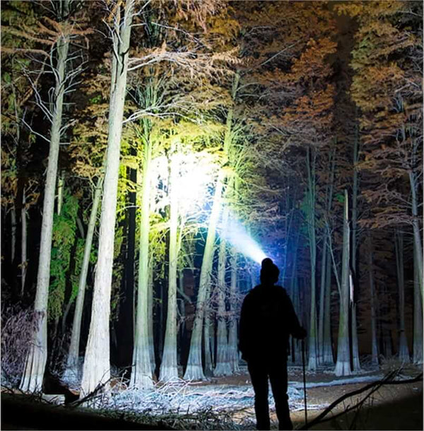 Person using high-power headlamp to illuminate a forest at night, showcasing lamp's 90,000 lumens brightness for outdoor activities.