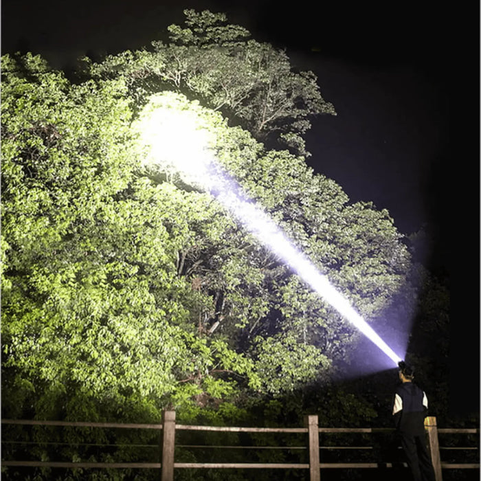 Une lampe frontale haute puissance illuminant un arbre, idéale pour le camping sauvage et l'exploration en plein air, mettant en avant sa luminosité de 90 000 lumens.