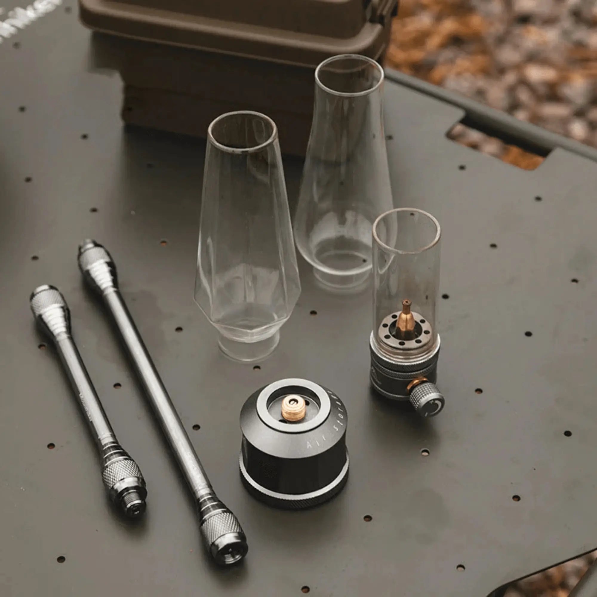 Pieces of a rechargeable camping gas lantern on a table, including glass covers and metal components for outdoor lighting setup.