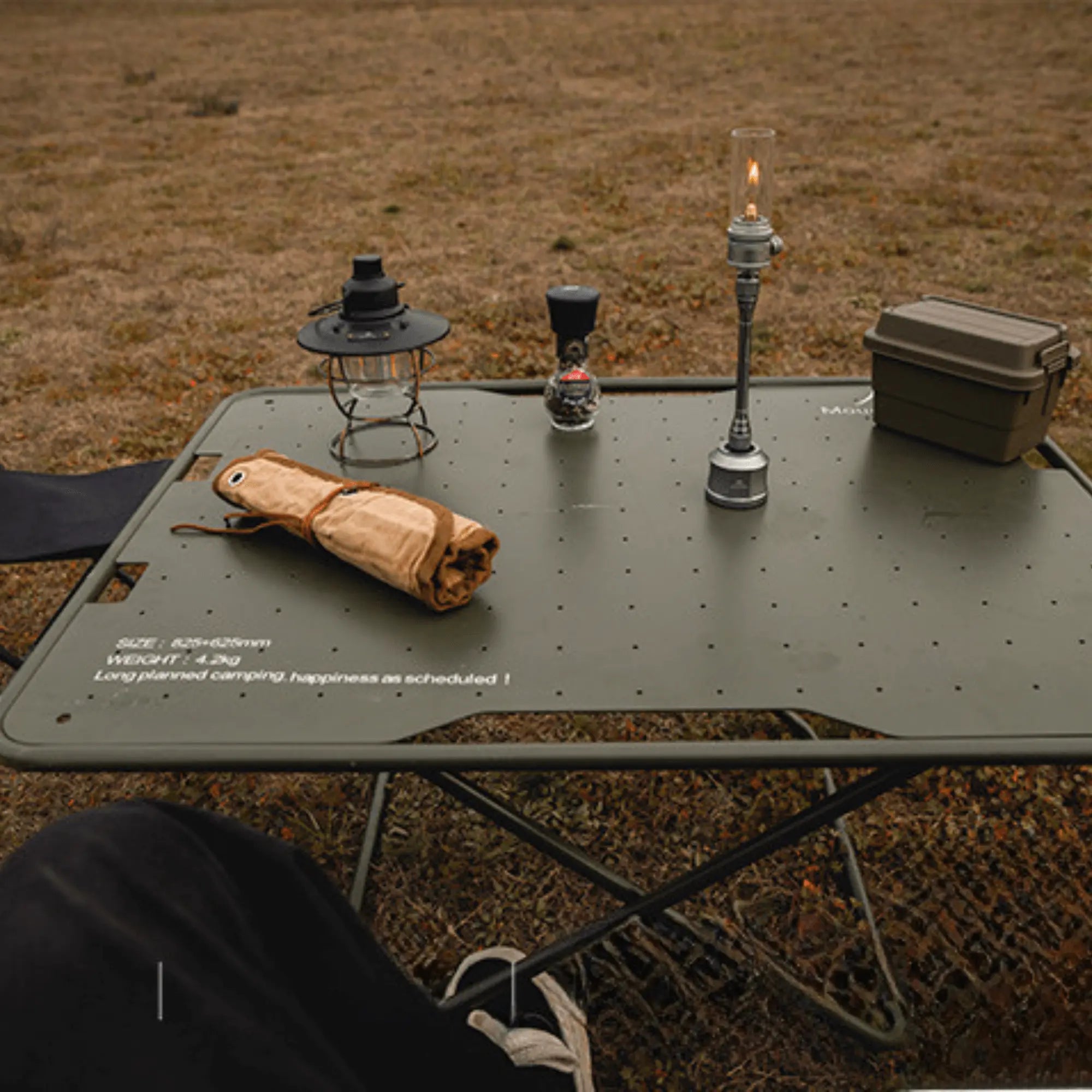 Outdoor camping setup with a gas lantern on a table, creating a warm ambiance. Includes camping gear and a scenic background field.