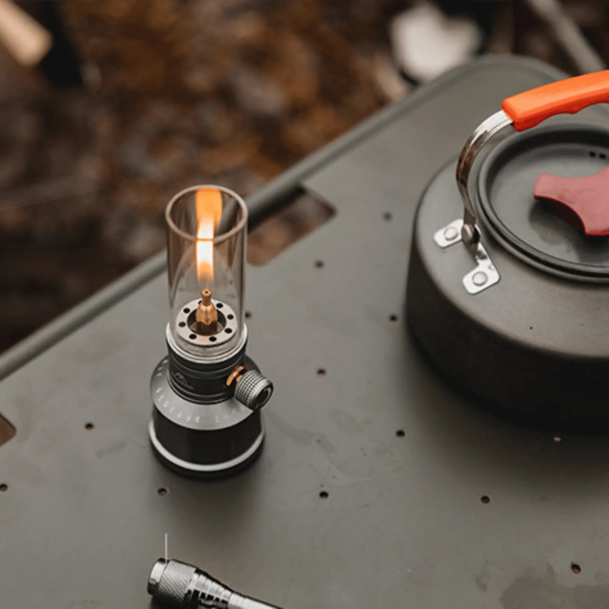Lampe lanterne à gaz de camping rechargeable émettant une lumière chaleureuse sur une table de camping avec une théière.