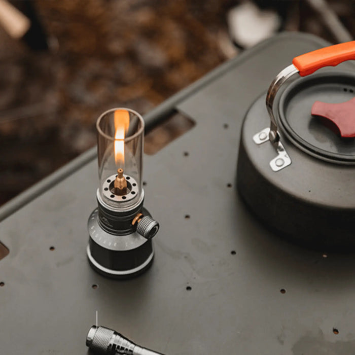 Lampe à gaz rechargeable émettant une lumière chaleureuse sur une table de camping avec une théière.