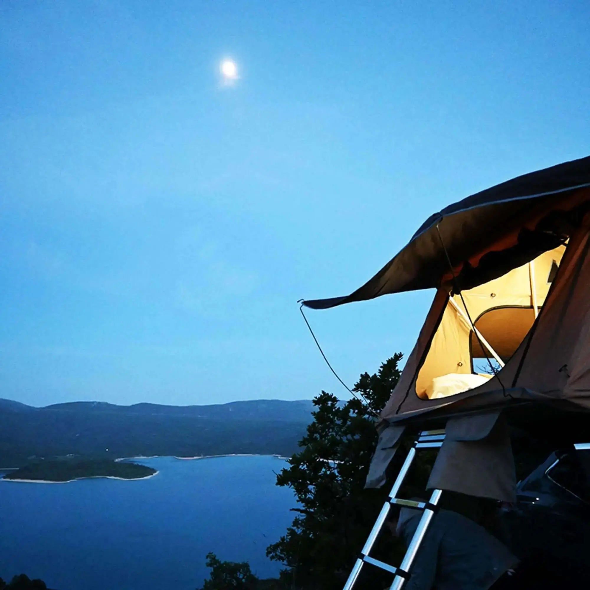 Rooftop tent illuminated by LED lights at dusk overlooking a scenic lake view, perfect for camping adventures.
