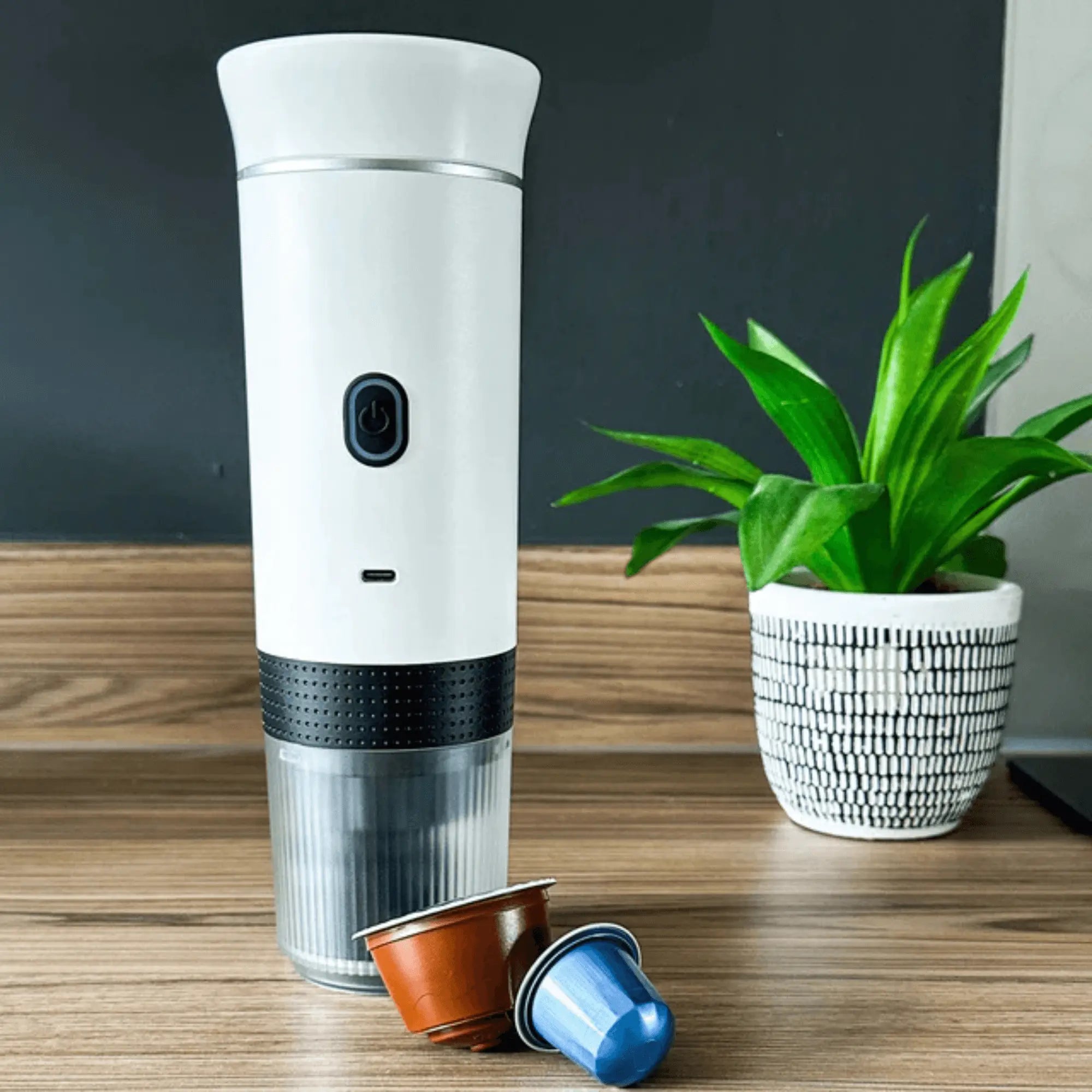 Portable electric coffee machine with capsules, perfect for espresso on the go, displayed on a wooden countertop.
