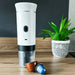 Machine à café électrique portable avec capsules, parfaite pour un espresso à emporter, exposée sur un plan de travail en bois.