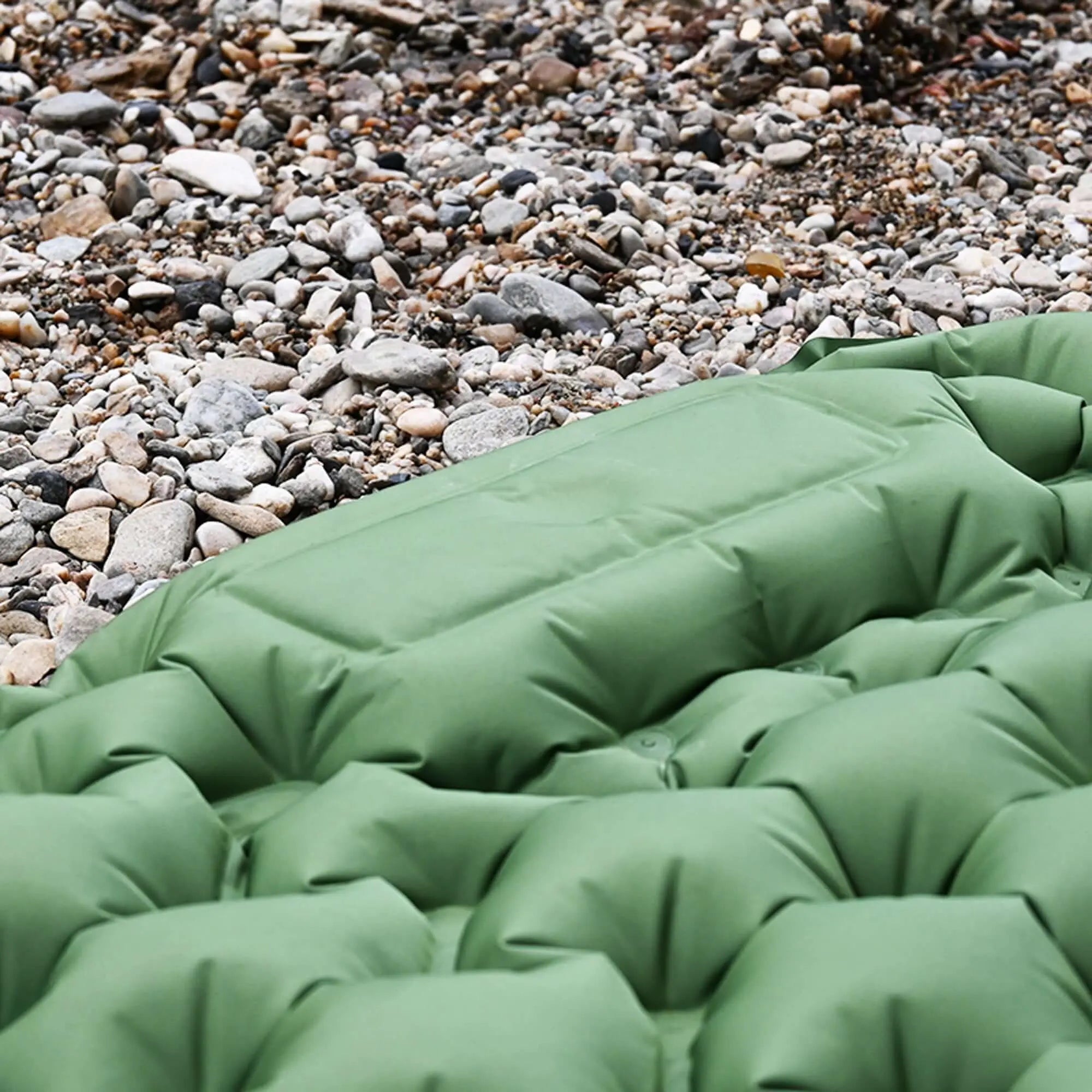 Close-up of green inflatable camping mattress on rocky ground, showcasing the supportive and comfortable air cell structure.