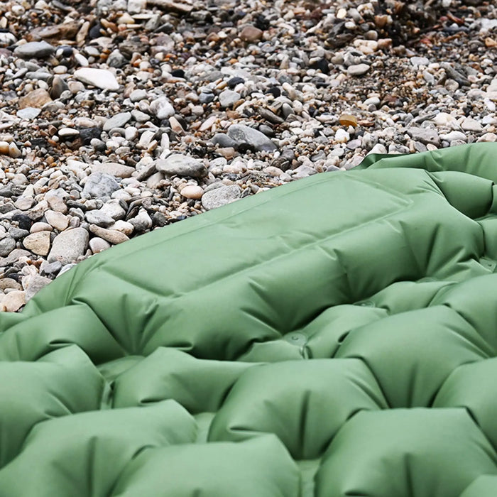 Gros plan sur un matelas de camping gonflable vert sur un sol rocheux, mettant en avant la structure des cellules à air, qui offre un soutien et un confort.