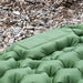 Gros plan sur un matelas de camping gonflable vert sur un sol rocheux, mettant en avant la structure des cellules à air, qui offre un soutien et un confort.
