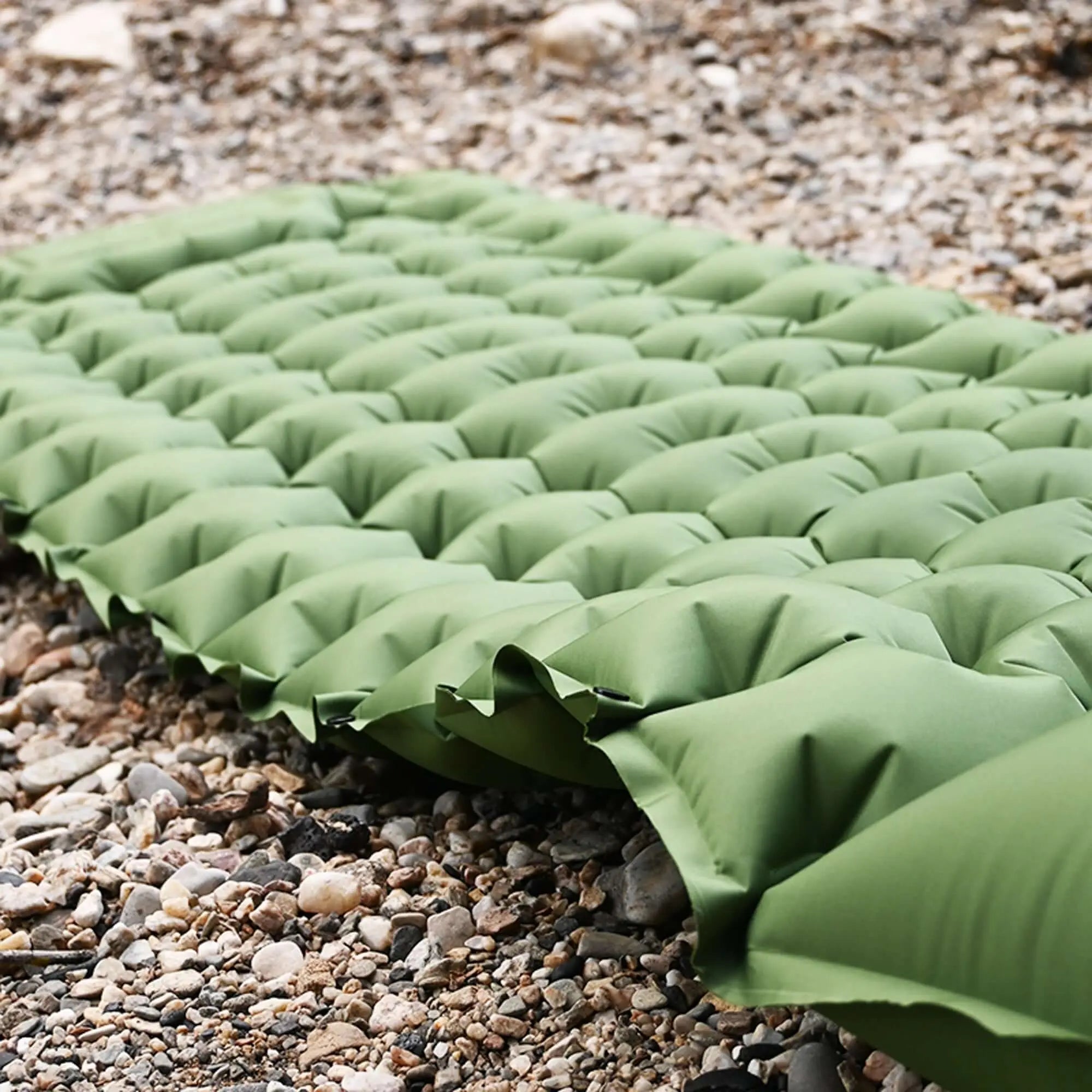 Green inflatable camping mattress on rocky ground, ideal for rooftop tents and outdoor comfort. Lightweight and space-saving design.