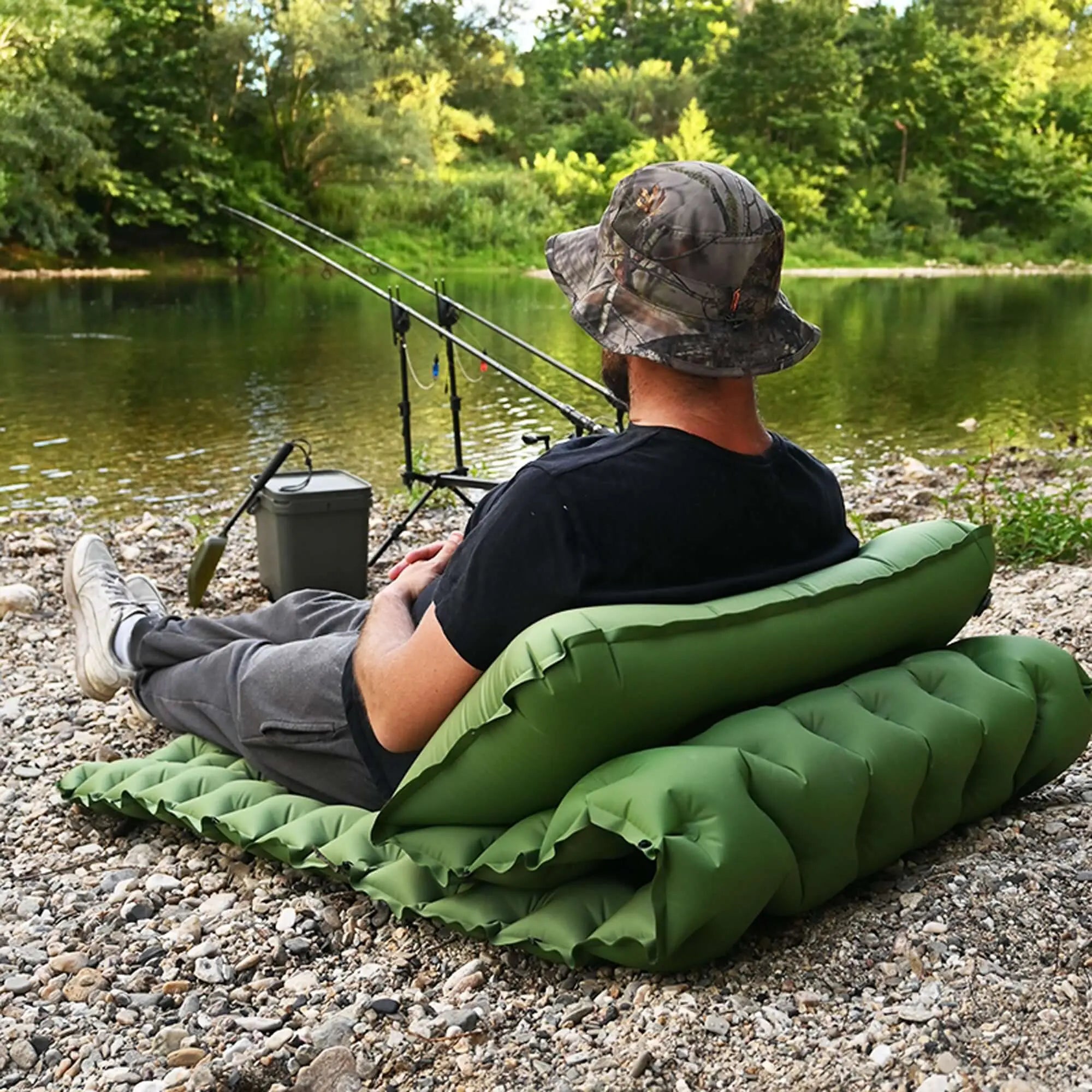 Person relaxing on inflatable camping mattress by a river, featuring built-in cushion and cellular structure for extra comfort.