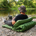 Personne se détendant sur un matelas de camping gonflable au bord d'une rivière, avec un coussin intégré et une structure cellulaire pour un confort supplémentaire.