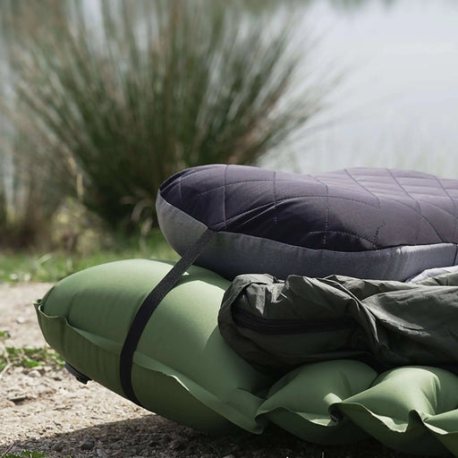 Oreiller de camping gonflable ultraléger, idéal pour le camping, posé sur un sol naturel près d'un étang, prêt à offrir un confort portable.