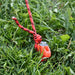Piquet de tente orange avec corde sur l'herbe, idéal pour une installation de camping sécurisée.