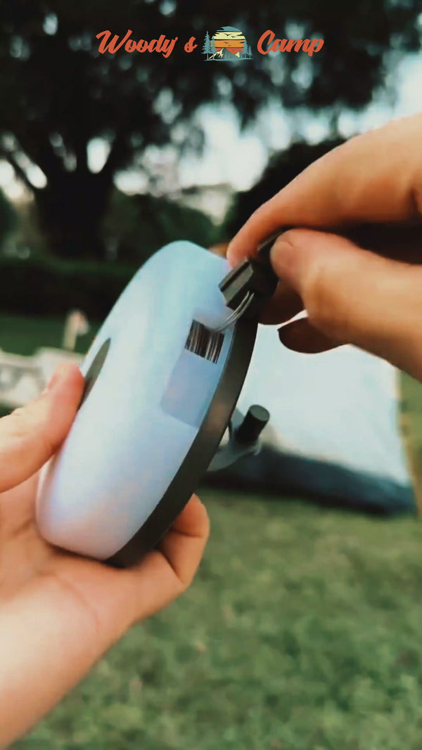 Person winding portable retractable LED string lights for outdoor camping use.