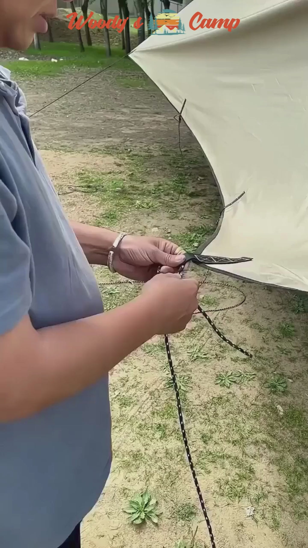 Person using a Serre-Corde Anti-Vent with pulleys to secure a tent in an outdoor camping setting.