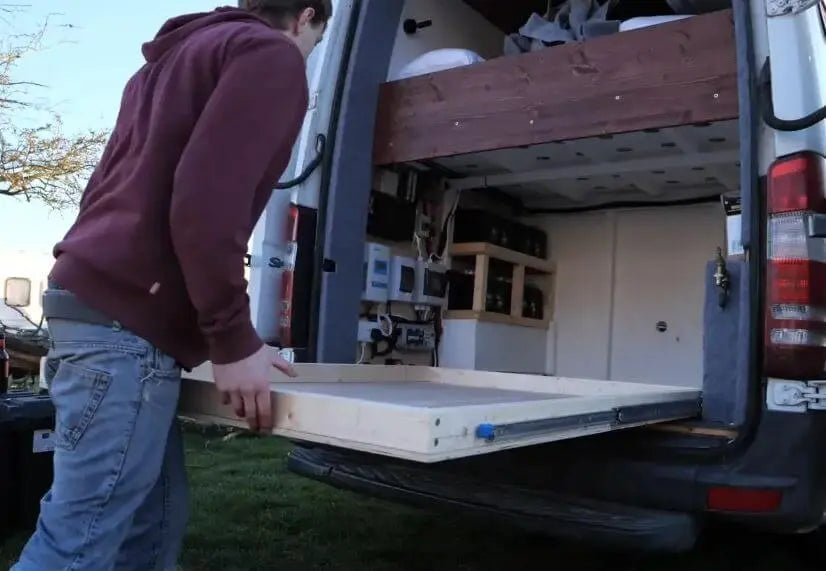 Person extending a sliding drawer with heavy-duty ball bearing glides in a camper van for efficient storage.