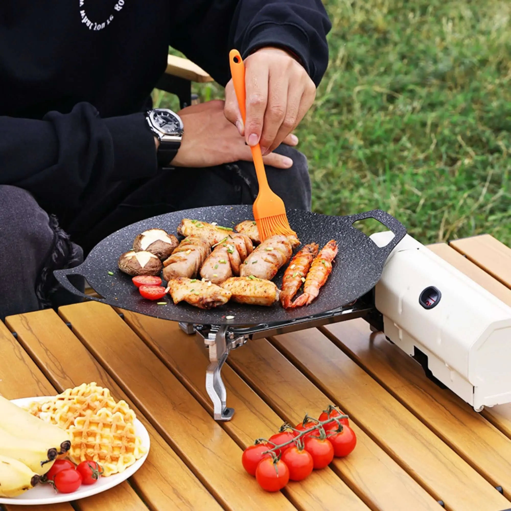 Portable camping stove in use, cooking various foods outdoors on a picnic table, showcasing versatile and compact design for outdoor cooking.