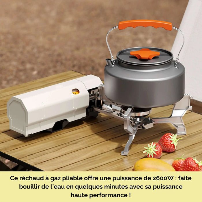 Réchaud de camping pliable sur table en bois avec bouilloire grise, prêt pour une cuisson rapide et efficace, idéal pour l'extérieur.