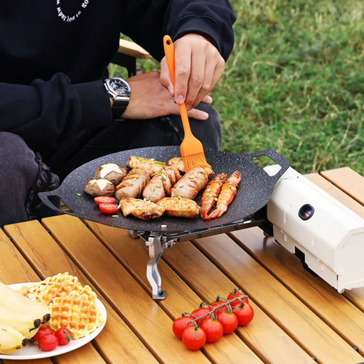 Réchaud de camping portable en utilisation, cuisinant divers aliments en plein air sur une table de pique-nique, mettant en valeur un design polyvalent et compact pour la cuisine en extérieur.