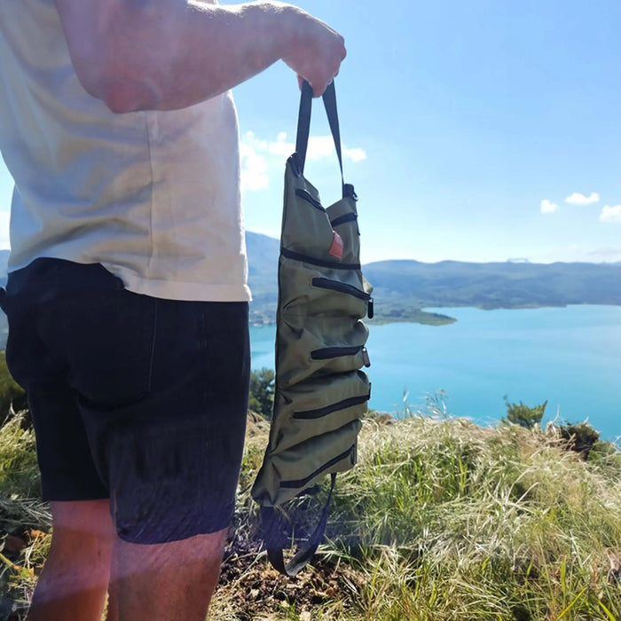 Une personne tenant un sac de rangement pliable pour le camping avec plusieurs compartiments, avec une vue pittoresque sur un lac.