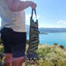 Une personne tenant un sac de rangement pliable pour le camping avec plusieurs compartiments, avec une vue pittoresque sur un lac.