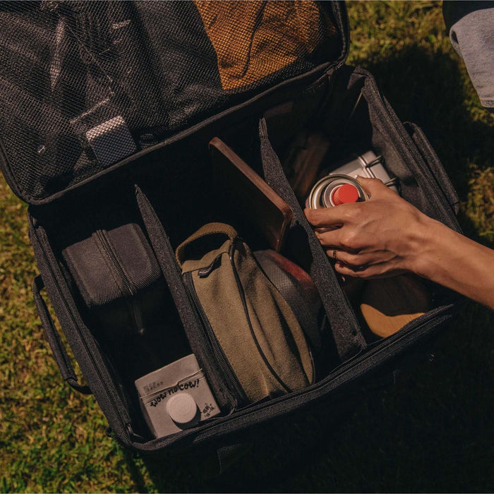 Une personne en train de ranger du matériel de camping dans une boîte de transport pliable avec un cadre en métal, mettant l'accent sur l'organisation et la commodité pour les activités de plein air.