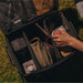 Une personne en train de ranger du matériel de camping dans une boîte de transport pliable avec un cadre en métal, mettant l'accent sur l'organisation et la commodité pour les activités de plein air.