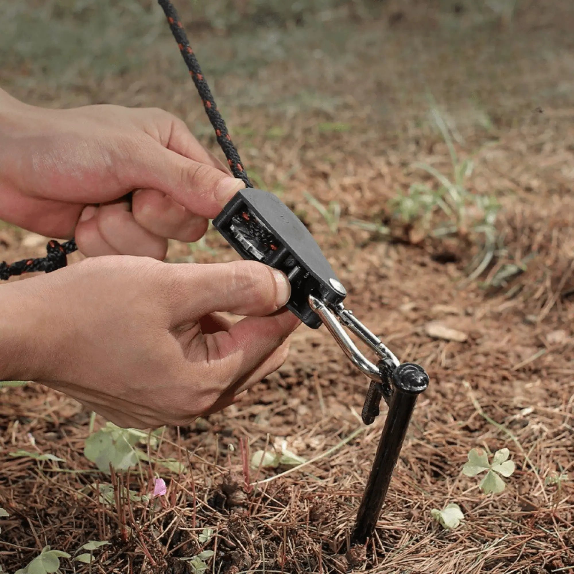Hands securing a camping rope with a 5-meter anti-wind pulley system in the ground for outdoor equipment stability.