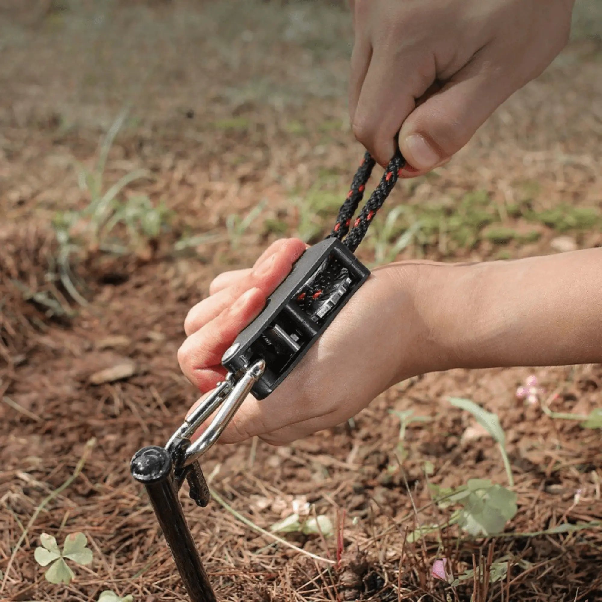 Hands using a Serre-Corde Anti-Vent with Pulley to secure camping equipment, demonstrating stability and easy setup in outdoor settings.
