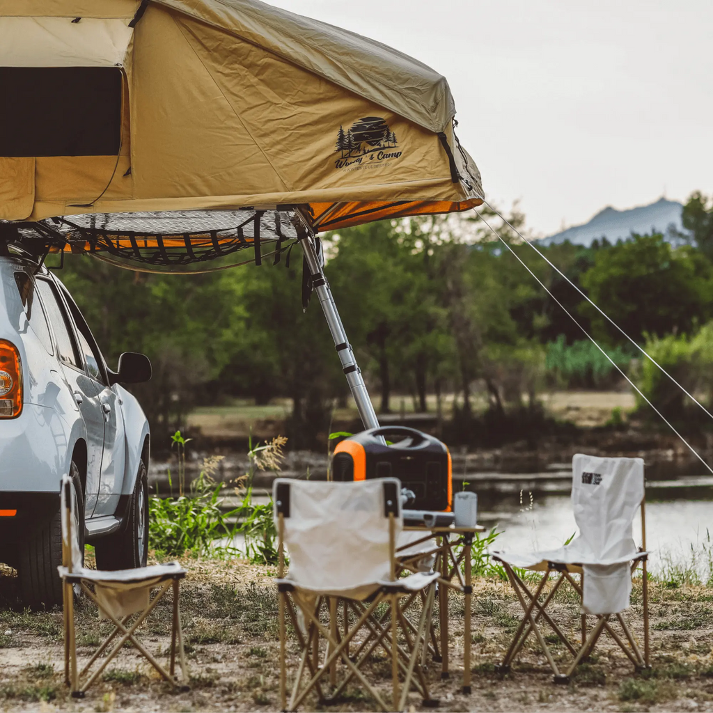 Camping setup with portable table and chairs by a car, ideal for picnics and outdoor events.