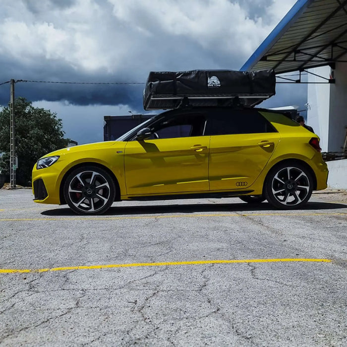 Voiture jaune avec une tente de toit et une housse en PVC pour un camping résistant aux intempéries, garée à l'extérieur sous un ciel nuageux.
