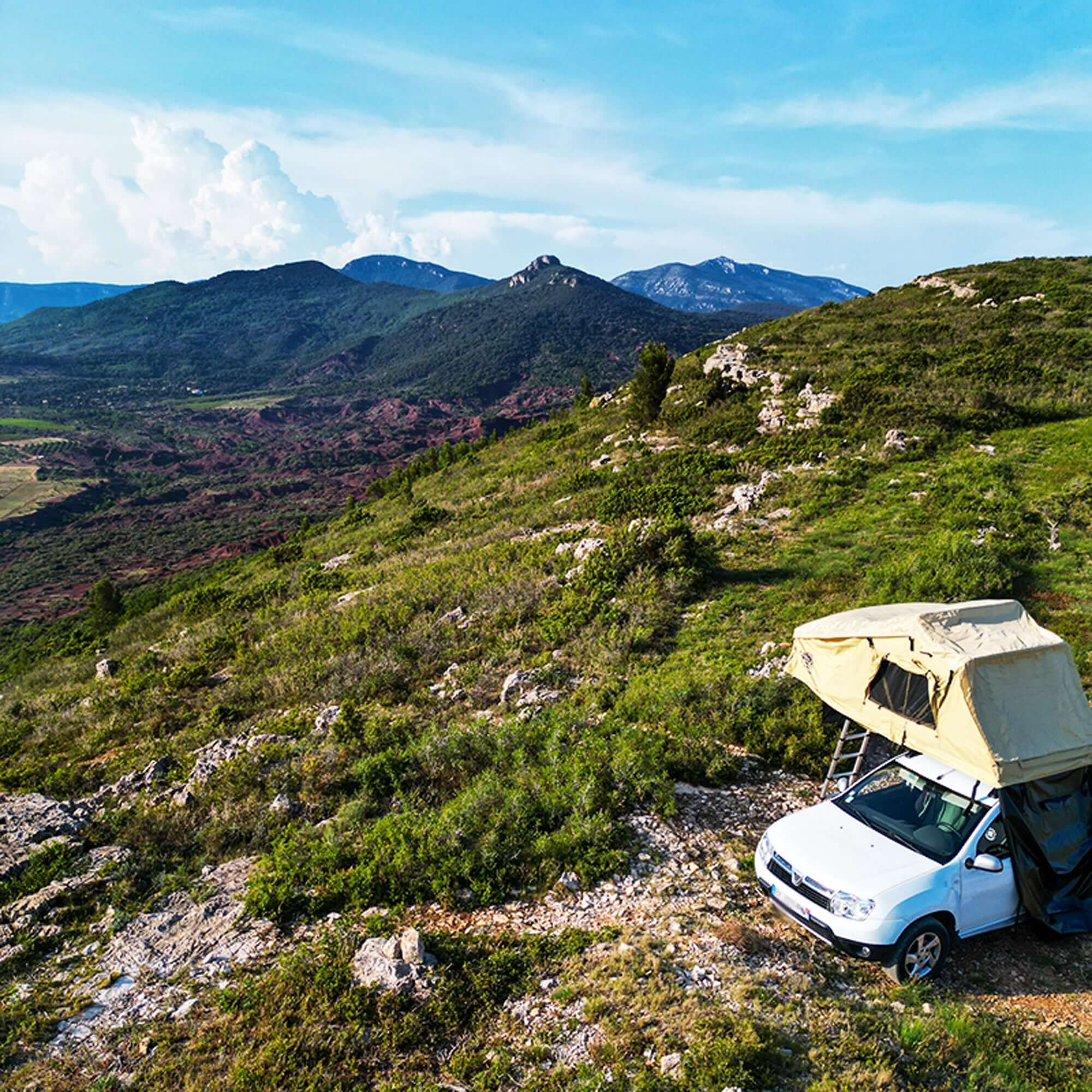 Car with roof tent set up on a hillside, surrounded by scenic mountainous landscape, ideal for outdoor camping adventure.