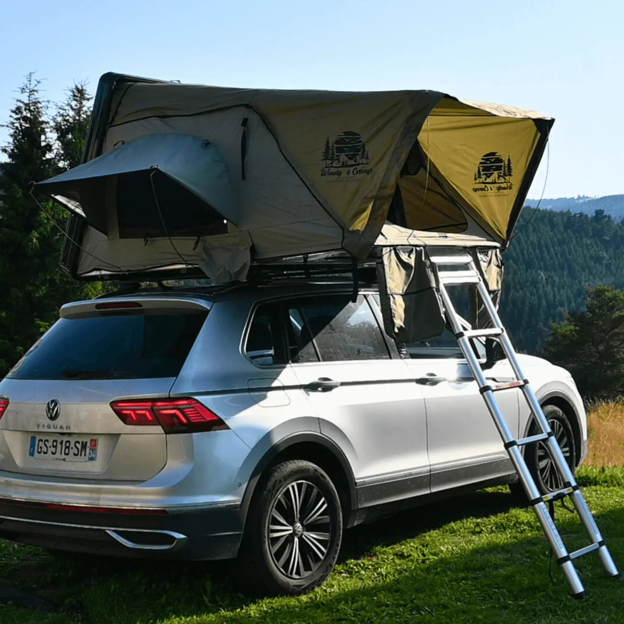 Car with rooftop hard shell tent and annex in outdoor setting, perfect for camping adventures.