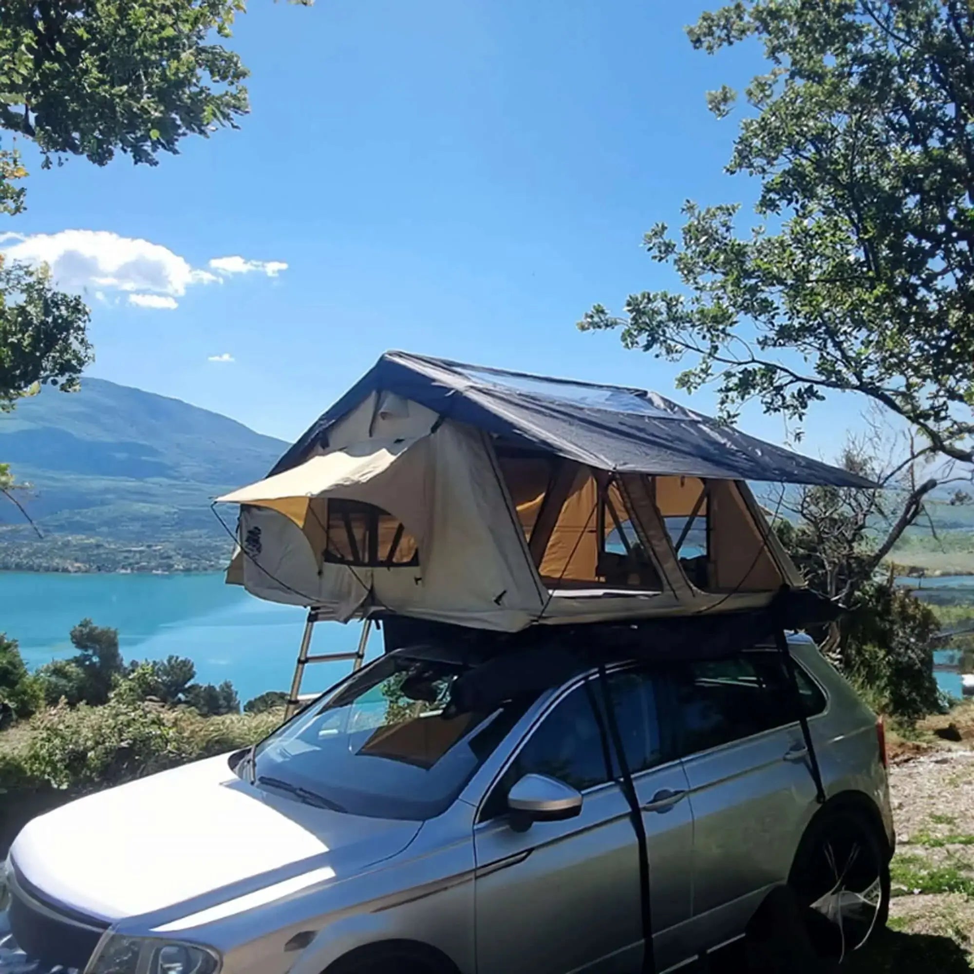 Roof-top tent for 4-5 people in beige and black on a car, overlooking a scenic lake and mountains.