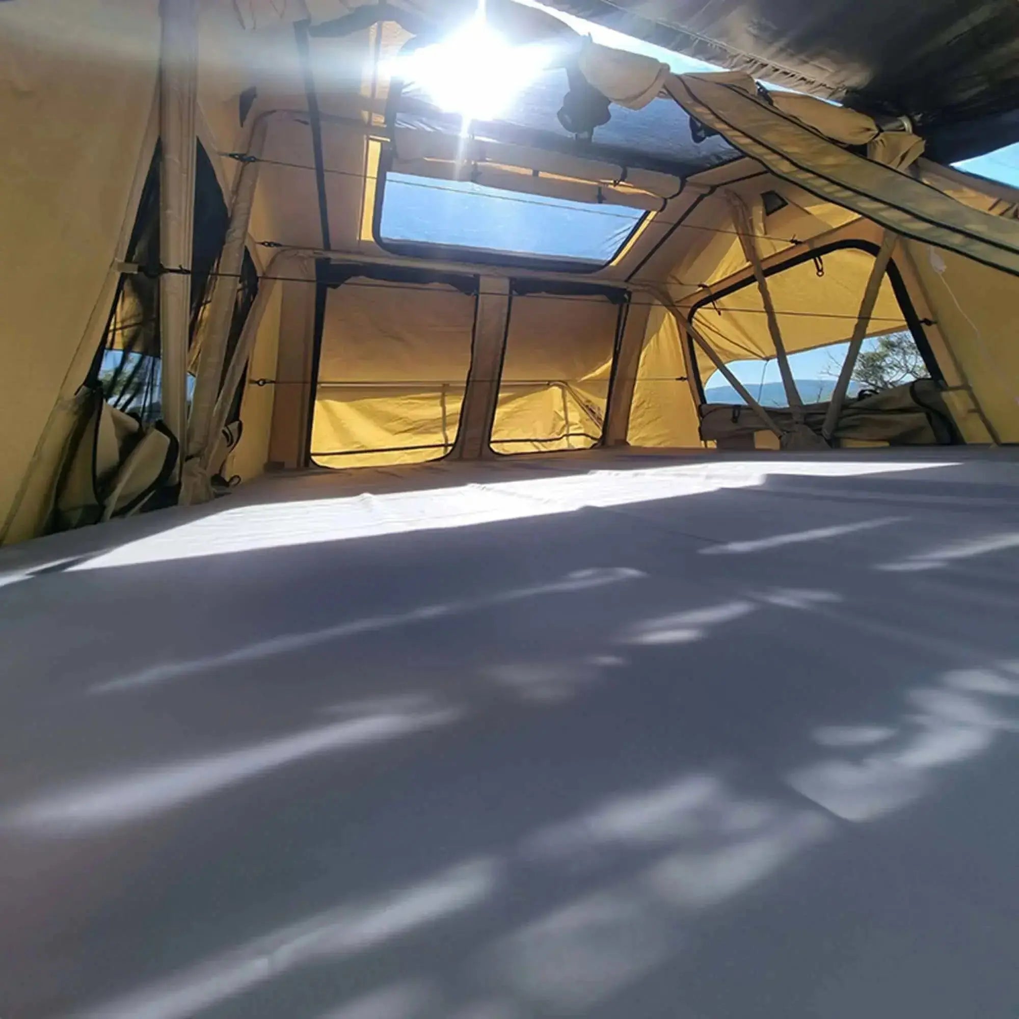 Inside view of a soft rooftop tent for 4-5 people, beige color with black top, sunlight streaming through windows, 2025 pre-order.