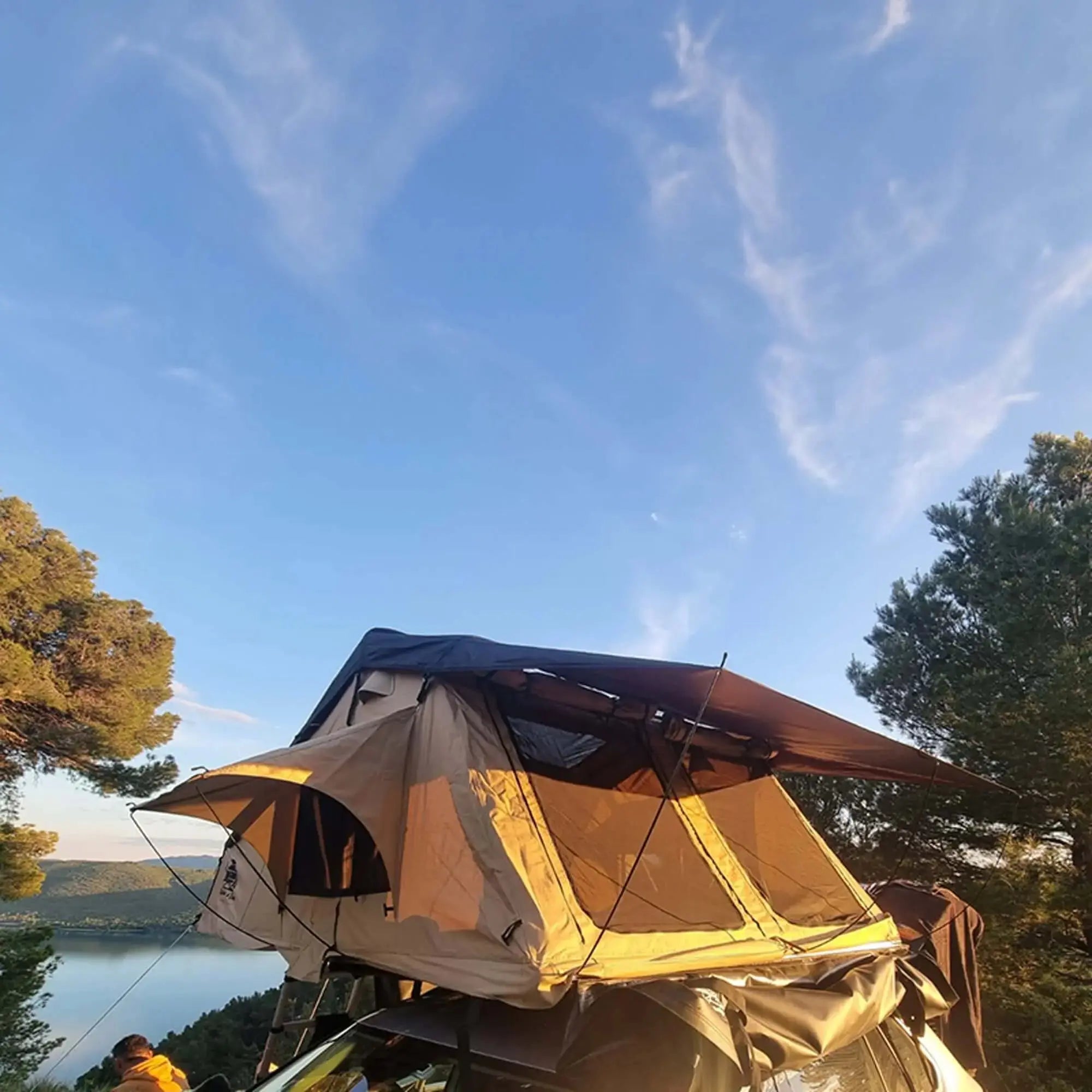 Roof tent for 4-5 people set up on a vehicle against a scenic backdrop of trees and sky.