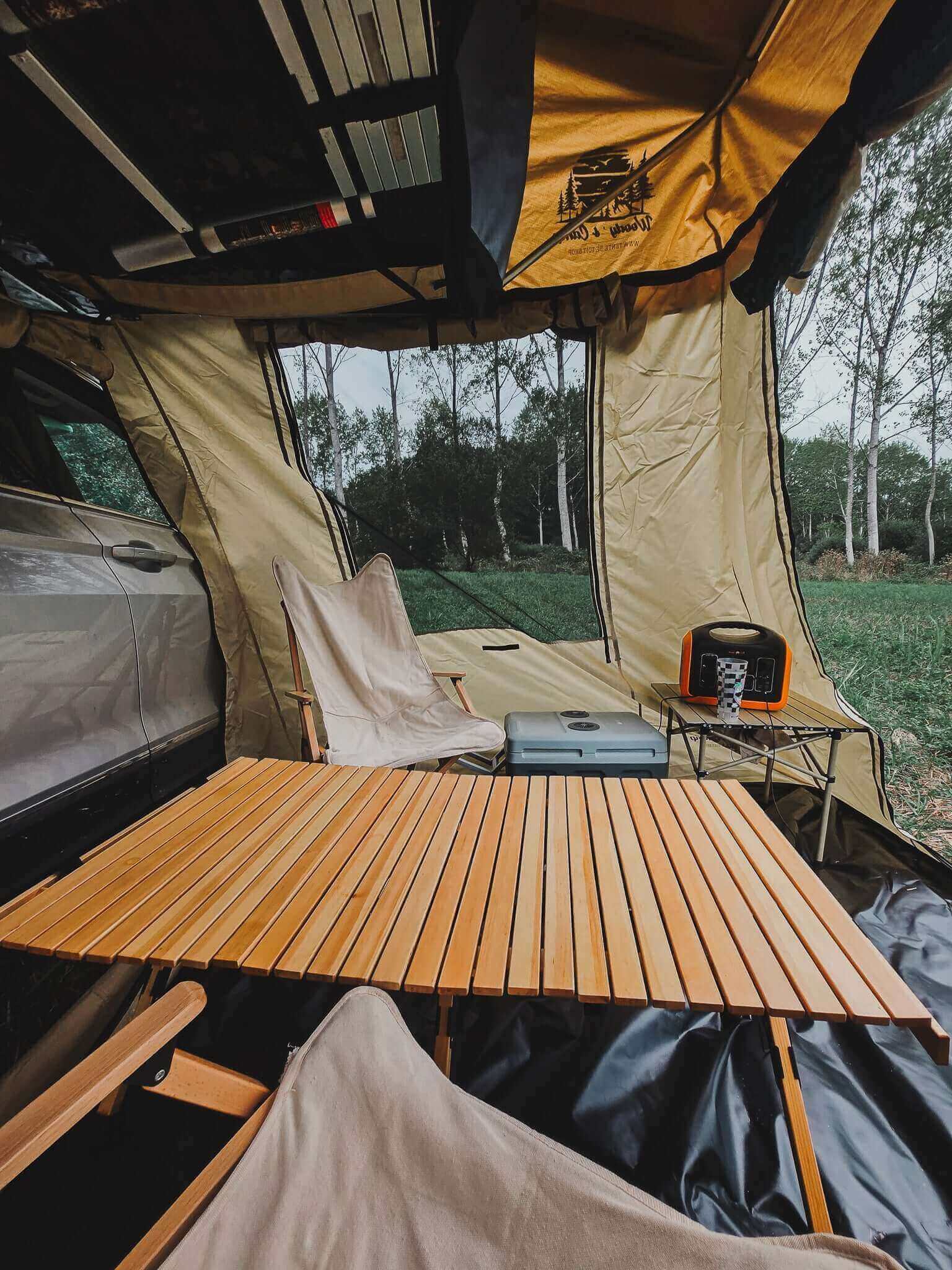 Cozy interior of a rooftop tent annex with wooden table and chairs, set up in a lush green outdoor setting.