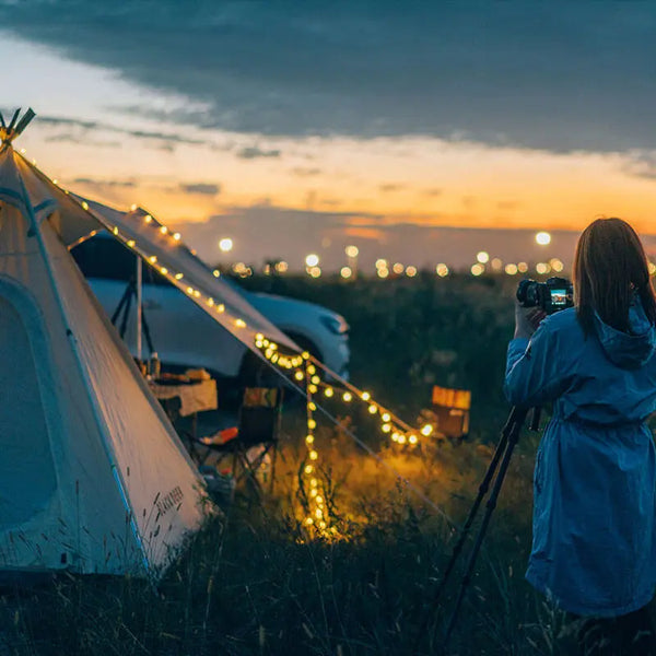 Camper photographing sunset with solar USB LED string lights on tent