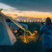 Un campeur photographiant le coucher de soleil avec des guirlandes LED solaires USB autour de sa tente.